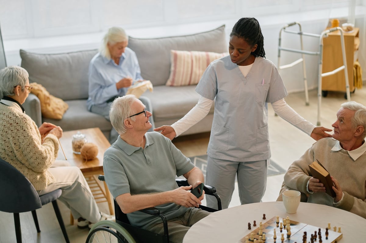 Nurse engaging with elderly residents at assisted living facility during activity time, promoting sense of community while seated at table