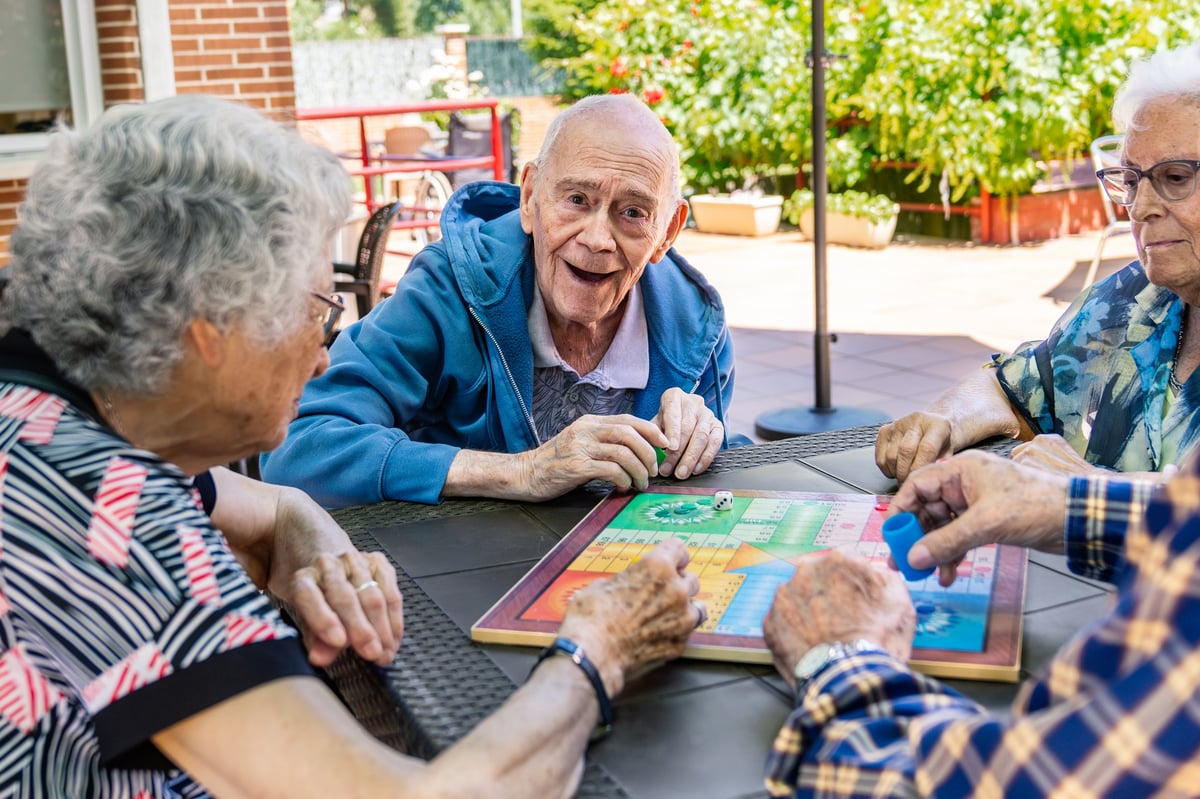 Senior adults enjoying a board game on a sunny patio, laughing and socializing in a retirement community